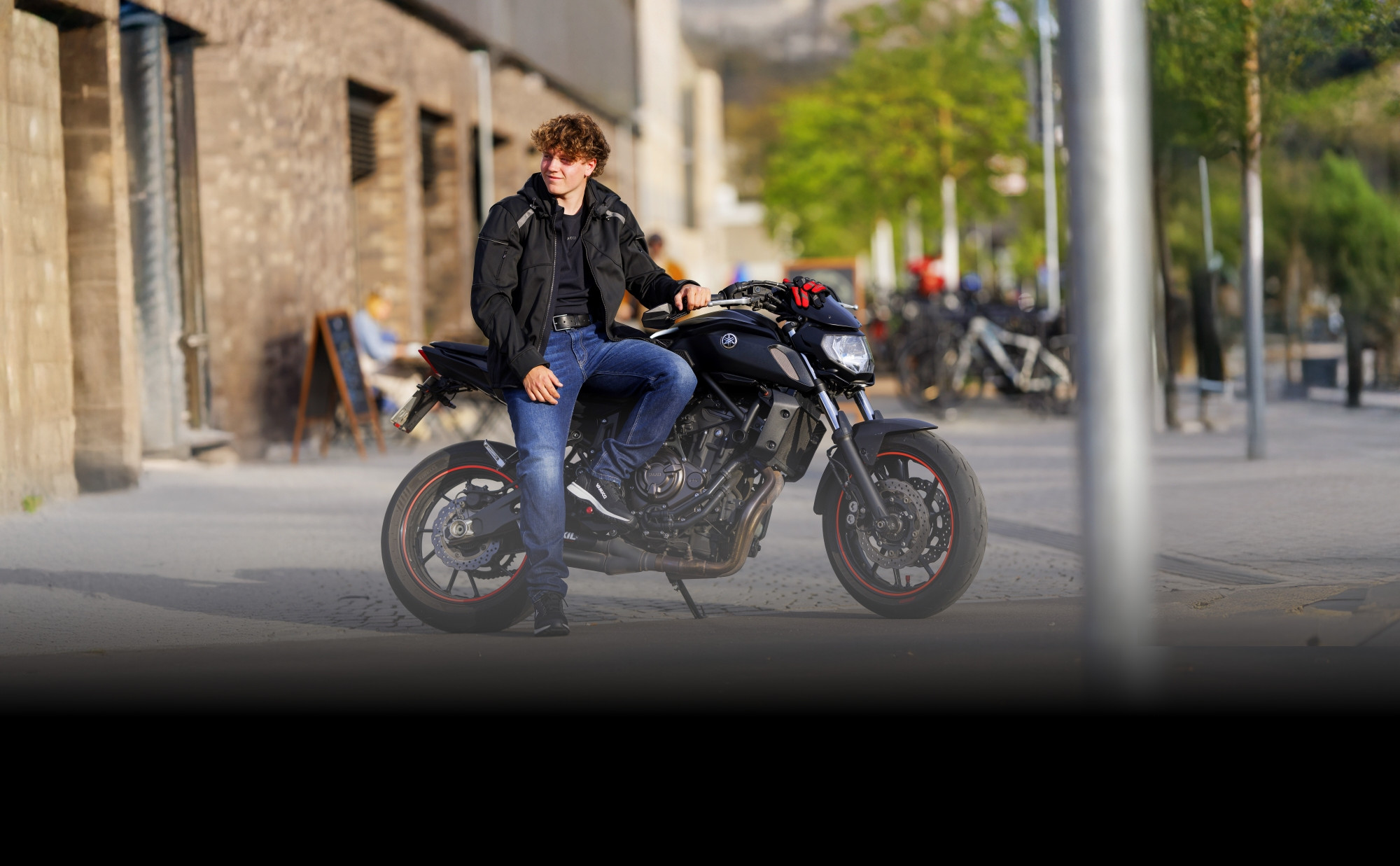 Motorradfahrer sitzt in Freizeitkleidung auf einem Naked Bike in einer urbanen Umgebung. Motorradbekleidung im Casual-Look