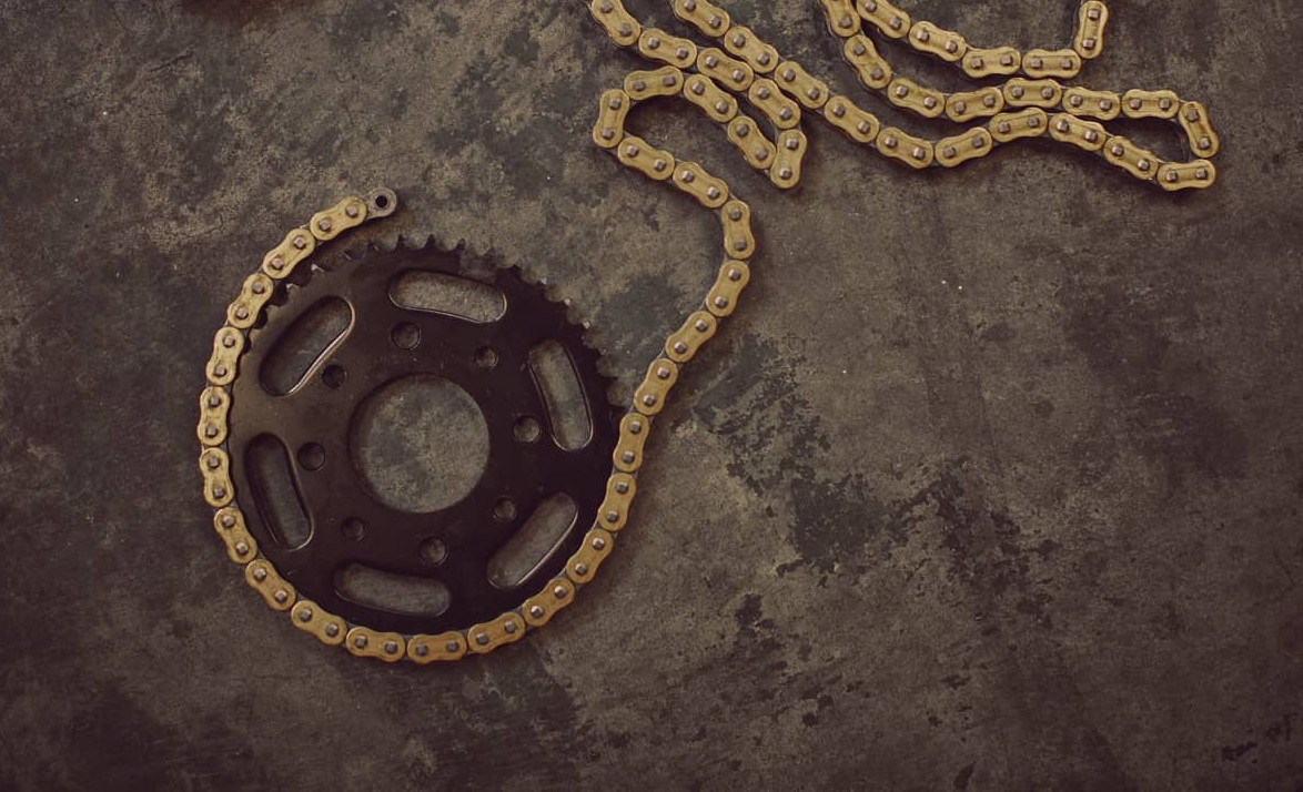 Detailaufnahme eines Motorradkettenantriebs mit Kettenrad und Antriebskette auf dunklem Untergrund.