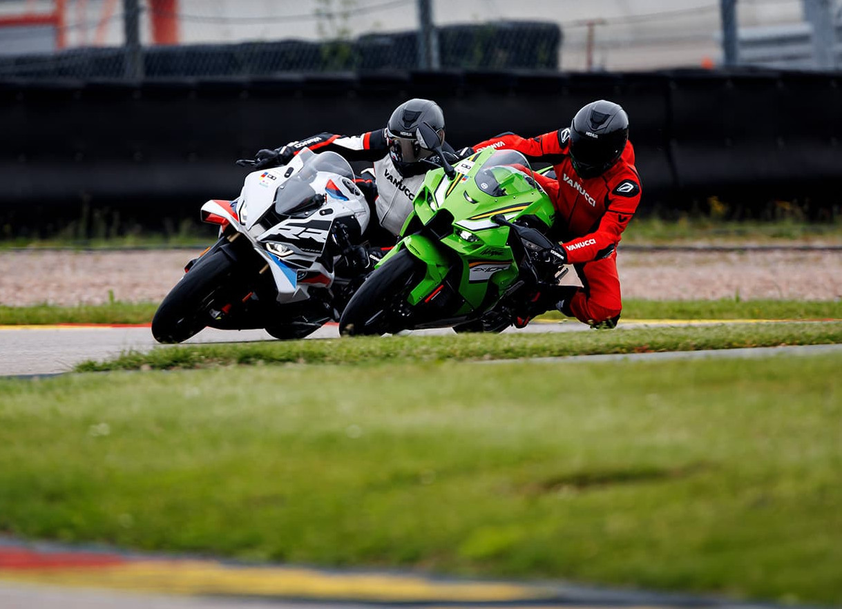 KI generiert: Das Bild zeigt zwei Motorradrennfahrer, die auf einer Rennstrecke in einer Kurve liegen. Beide tragen Schutzausrüstung und sind in unterschiedlichen Rennanzügen, wobei einer grün und der andere rot gekleidet ist.