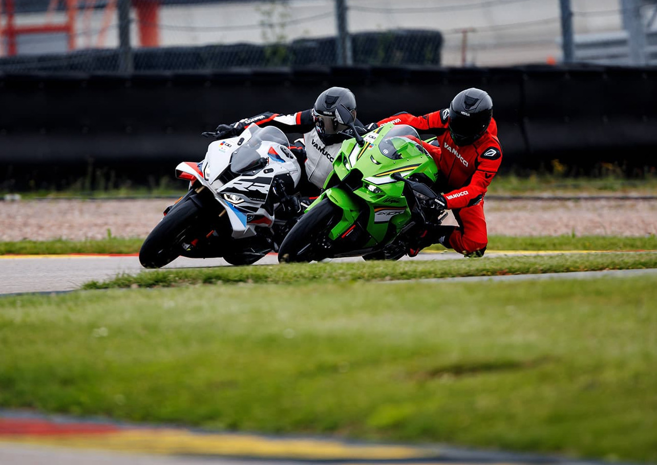 KI generiert: Das Bild zeigt zwei Motorradrennfahrer, die auf einer Rennstrecke in einer Kurve gegeneinander kämpfen. Sie tragen bunte Rennanzüge und Helme und sind in einer dynamischen, leicht geneigten Position, um die Kurve zu meistern.
