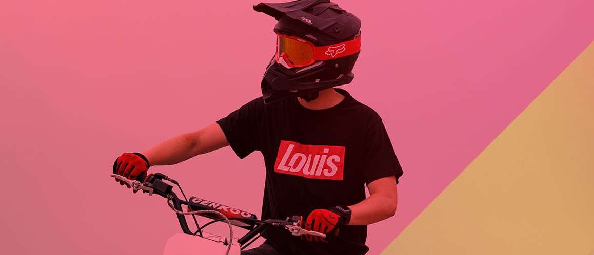 Person mit Motorradhelm auf Motorrad und schwarzem Louis‑T‑Shirt vor Farbverlauf mit Schriftzug ‚RIDE IT. LIVE IT. WEAR IT.
