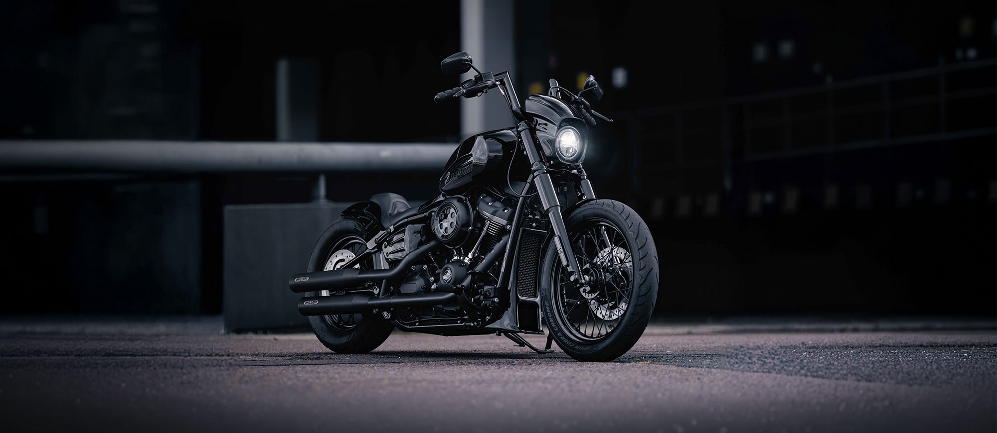 KI generiert: Die Hauptmotiv der Aufnahme ist ein schwarzes Motorrad mit Chrom-Elementen, das auf einer StraĂe steht. Im Hintergrund sind unscharfe BĂ€ume und ein GebĂ€ude zu erkennen.