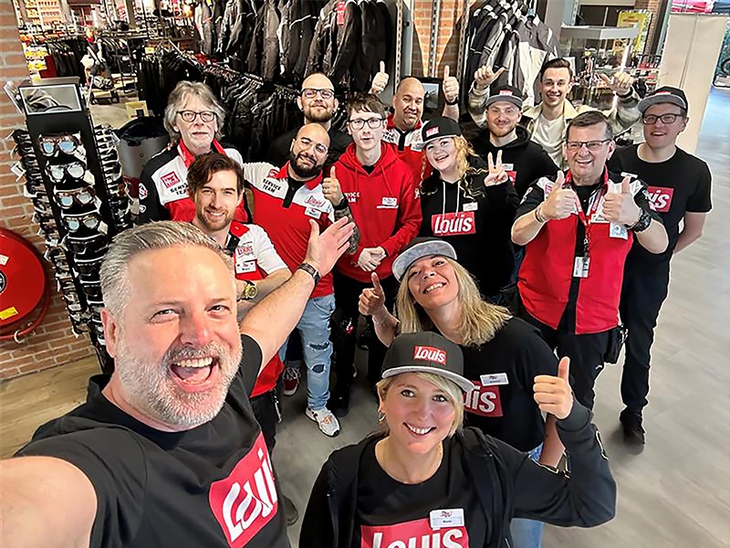KI generiert: Das Bild zeigt eine Gruppe von Menschen in einem Hockey-Shop, die sich vor einem Regal mit Hockey-Trikots und -Helmen versammelt haben. Die meisten Personen tragen Hockey-Trikots und wirken fröhlich und zufrieden, was auf eine positive Stimmung hindeutet.